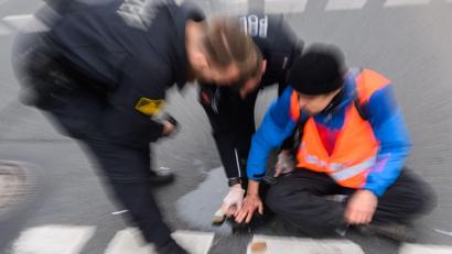 Bild: Julian Stratenschulte/dpa
Polizisten versuchen festgeklebte Hände von Aktivisten von der Straße abzulösen.