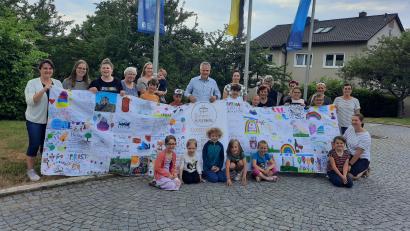 Bild: Gemeindebücherei/exb
Das Bücherei-Team übergibt Bürgermeister Thomas Meiler (Mitte) zusammen mit kleinen und großen Lesern und der Kindergartenleitung das Banner zum 1075. Geburtstag der Gemeinde.
