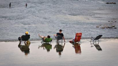 Bild: Karl-Josef Hildenbrand/dpa
Junge Männer sitzen auf Campingstühlen im seichten Wasser oberhalb des Lechwehrs.