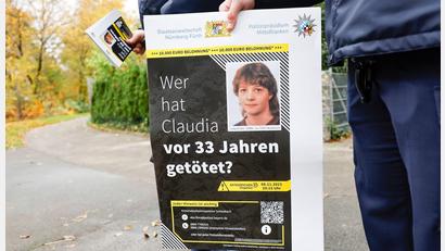Bild: Daniel Löb/dpa
Ein Polizist mit einem Plakat zum Mordfall von 1990 in Röthenbach an der Pegnitz.