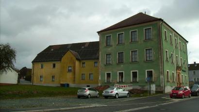 Bild: bjp
Schluss mit der Schotterwüste: Begrünt und barrierefrei soll sich der Klosterhofparkplatz (links) in naher Zukunft präsentieren. Die symmetrische Ästhetik der Westfassade des "Hauses der Heimat" (rechter Bildrand) soll erhalten bleiben. Die Renovierungsbedürftigkeit des gut 120 Jahre alten Gebäudes ist unübersehbar.