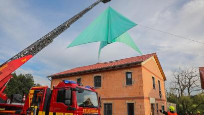 Bild: Wolfgang Steinbacher
Die Drehleiter der Feuerwehr Hirschau hievt das hellgrüne Folien-Notdach über den Neubau, der als Übungsobjekt dient.