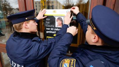 Bild: Daniel Löb/dpa
Polizisten hängen das Plakat zum Cold-Case von Claudia Obermeier an einer Glasscheibe auf.