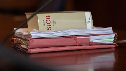 Symbolbild: Swen Pförtner/dpa
Das Strafgesetzbuch und Akten liegen in einem Gerichtssaal auf dem Tisch.