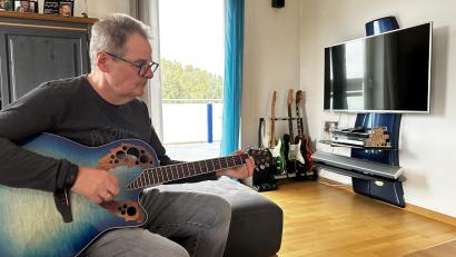 Bild: kle
Egid Spies sitzt mit seiner Gitarre auf dem heimischen Sofa. Seit einer Covid-Infektion hat er starke kognitive Probleme. Plötzlich fielen ihm die über Jahrzehnte erlernten Gitarrengriffe nicht mehr ein.