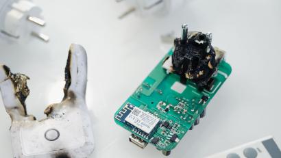 Symbolbild: Marius Becker /dpa
Eine verbrannte Funksteckdose liegt in einem Schaukasten. Hätte man einen technischen Defekt frühzeitig erkennen können?