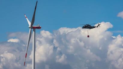 Symbolbild: Jan Woitas/dpa
Ein Bundeswehrhubschrauber vom Typ Sikorsky CH-53 fliegt mit Löschwasser zur Waldbrandbekämpfung an einem Windrad vorbei.