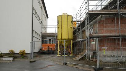 Bild: bey
Zwischen der Schule (links) und der Mehrzweckhalle (rechts) muss das Stahlrohr für die Aufnahme von Kanal und Wasserleitung verlegt werden. Es ist ein echter neuralgischer Punkt, weil das Stahlrohr tiefer gelegt werden muss als die Fundamente der beiden Gebäude in den Boden verbaut sind. Außerdem ist das Grundwasser ein nicht zu übersehendes Problem.
