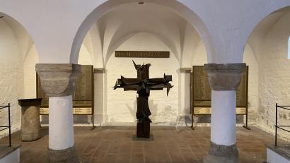 Bild: aub
Das durch seine schlichte und zugleich eindrucksstarke Form wirkende Kreuz in der Nikolauskirche findet in Kulturkreisen große Anerkennung. Ursprünglich bot der steinerne Ambo links Platz für das Buch mit den Namen der Gefallenen. Entgegen dem Ursprungskonzept des Künstlers wurden später die alten Holztafeln hinzugefügt.