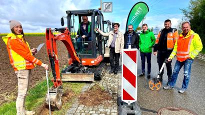 Bürgermeister Uwe König hebt unter fachmännischer Beobachtung mit dem Bagger die erste Vertiefung für das Glasfaserkabel in Thansüß aus.