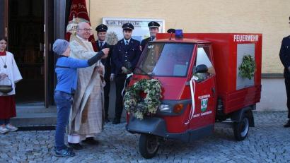 Bild: Bernhard Zimmet/exb
Pfarrer Wilhelm Bauer erteilt, unterstützt von Feuerwehrnachwuchskraft Felix Heuberger, der für Festumzüge umgebauten „Feuerwehr-Ape“ den kirchlichen Segen.