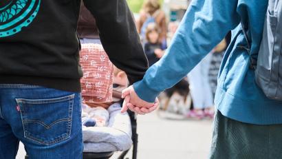 Symbolbild: Annette Riedl/dpa
Eltern halten Händchen, während sie mit ihrem Baby im Kinderwagen über einen Markt gehen.