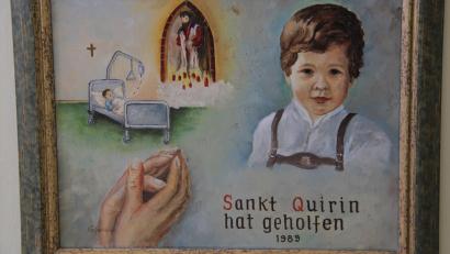 Bild: prh
29 Votivbilder zeugen in der Votivkapelle von St. Quirin von tiefer Dankbarkeit für die Erhörung von Gebeten. Eines der jüngsten Werke ist dieses Bild von 1989. Damit dankt die Familie für die Heilung eines Buben von Leukämie.
