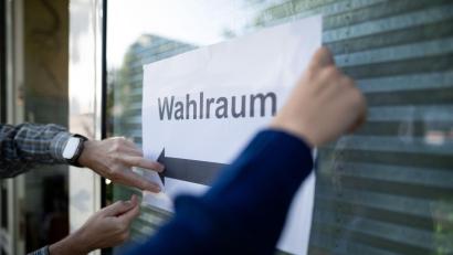 Bild: Fabian Strauch/dpa
Wahlhelfer hängen einen Zettel, auf dem „Wahlraum“ steht, auf.