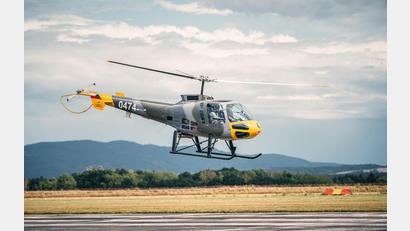 Bild: Ultralight Club Cheb
Ein grauer und gelber Hubschrauber mit der Nummer 0474 schwebt knapp über der Landebahn vor einer malerischen Landschaft mit Bergen und Wolken am Himmel beim Flugtag Eger (Cheb) 2024.