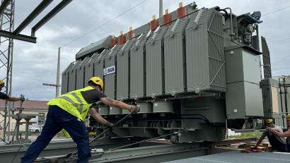 Bild: mgo
Der neue Trafo wiegt 56 Tonnen und kostet eine Million Euro. Zwei Bauarbeiter ziehen den Koloss mit zwei Seilwinden vom Tieflader auf das Fundament.