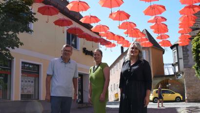 Bild: bö
Ein Großteil der Schirmstraße in Schmidmühlen ist mit neuen Regenschirmen nachgebessert worden. Die Sparkasse Amberg-Sulzbach hat die Aktion mit über 2000 Euro unterstützt (von links): Bürgermeister Peter Braun mit Anna Pitera und Melanie Misral von der Sparkasse Amberg-Sulzbach.
