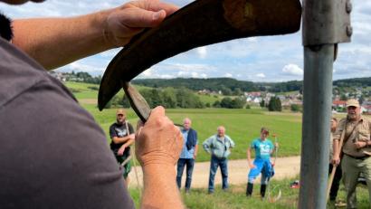 Bild: Heike Unger
So wird die Sense wieder scharf: Zwischendurch greift Experte Markus Achhammer auf dem Feld zum Wetzstein und zeigt seinen Kursteilnehmern, wie sie ihn richtig ansetzen („schön flach“), damit es klappt mit dem Schärfen.