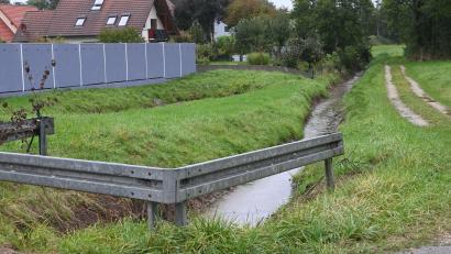 Bild: gf
Der Gebenbach ist bis zum Durchlass am Urspringer Weg gesäubert, ebenso das Regenüberlaufbecken (links vor dem Zaun). Im hinteren Bereich jedoch reicht die Bepflanzung bis an den Gebenbach heran, obwohl nach ursprünglichen Planungen diese Fläche entlang des Gebenbachs freizuhalten ist.