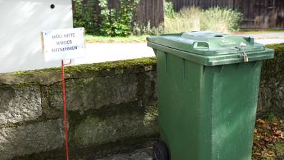 Bild: bkr
An der Stelle der Mülltonne für Plastikmüll steht nun ein Schild mit der Aufschrift: „Müll bitte wieder mitnehmen“. Die grüne Mülltonne daneben für Grablichter und der Container für Grüngut bleiben von der Maßnahme ausgeschlossen.