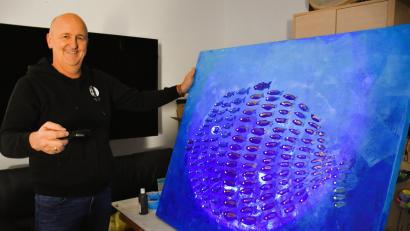 Bild: ubb
Jürgen Frischholz zeigt als Beispiel eines der fluoreszierenden Gemälde, das er selbst gemalt hat. Das Bild gibt es auch bei der Ausstellung zu sehen. Bei entsprechend richtiger Leuchttechnik wird der Effekt natürlich weit eindrucksvoller herausgearbeitet sein.