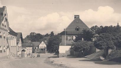 Bild: Archiv Werner Robl
Der Pfarrhof am Kirchplatz in Wiesau befindet sich in Nachbarschaft des Anwesens Stefflwirt (links im Bild). Darunter - in Richtung Tal - erkennt man den ehemaligen (heute deutlich veränderten) Aslhof. Unten sieht man das inzwischen verschwundene Lebensmittelgeschäft Härtl. Aus den Bäumen (rechts oben) spitzt der Turm der Kreuzbergkirche hervor.