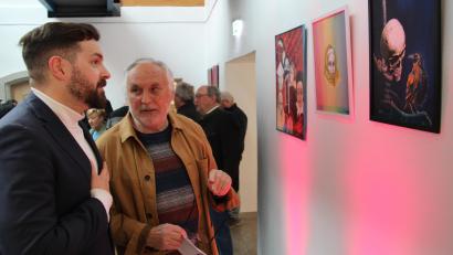 Bild: prh
Der Neustädter Maler Ernst Umann (rechts) erklärt Bürgermeister Sebastian Giering bei der Vernissage im Foyer des Rathauses sein Bild "Der Tod und der Rabe".