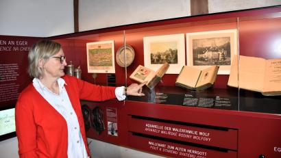 Bild: ubb
Tourismusleiterin Ursula Stingl zeigt auf das Hochzeitsbuch, das mit handgemalten Bildern bestückt ist und damit sehr wertvoll ist. Ab sofort gehört es zu den Ausstellungstücken des Sengerhofes.