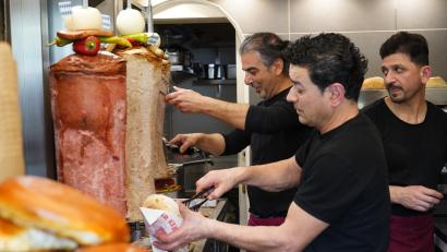 Bild: kaz
Marco Cakmak (links) bietet neben dem Leberkäs-Döner jetzt auch Varianten mit Weiß- und Bratwurst an. Mit seinem Mitarbeiter Turhan Bakir (Mitte) schneidet er das Brät vom Spieß. Huseyin Cakmak verpackt die Bestellungen.