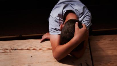 Symbolbild: Annette Riedl/dpa
Ein Kind versteckt sein Gesicht unter seinen Armen und liegt mit dem Kopf auf einem Tisch. Körperliche und emotionale Misshandlungen von Kindern können weitreichende Folgen haben.