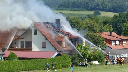 Bild: lgc
Aus dem Dachstuhl des Wohnhauses quellen dunkle Schwaden, während Feuerwehrleute gegen die Flammen ankämpfen.