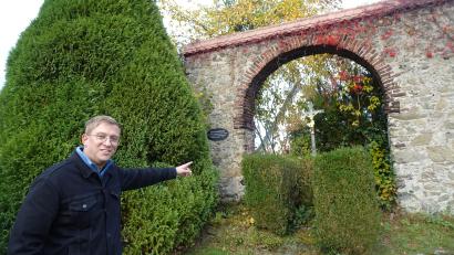 Bild: ui
Tobias Knauer weist auf den Grabstein des Kirchenmalers Thaddäus Rabusky, der unter dem Eingangstor des ehemaligen fürstlichen Gartens in Neustadt/WN steht. Die zu wuchtig gewordene Zypresse hinter Knauer kommt weg.
