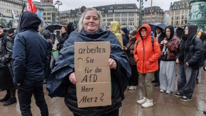 Bild: Markus Scholz/dpa
Eine Demonstrantin in Hamburg stellt auf einem Pappschild eine Frage an Bundeskanzler Friedrich Merz (CDU).