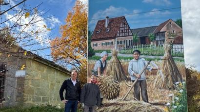 Bild: Elfriede Winter 
Bürgermeister Hans-Jürgen Strehl mit dem Künstler Markus Ronge vor der Ostseite mit dem Goglhof als Motiv. Wer von Süden kommt sieht die Edelsfelder Windräder, auf der Westseite grüßen die beiden Ortskirchen und im Norden tanzt ein Kirwapaar um den Kirwabaum.