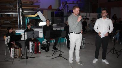 Bild: Bernhard Piegsa
Als Gastgeber begrüßte Schreinereiinhaber Sebastian Hösl (stehend, links) die rund 200 Besucher des Werkstattkonzerts, das Jonas Plössner (rechts) begleitete. Im Hintergrund das Speichersdorfer Akkordeonensemble.