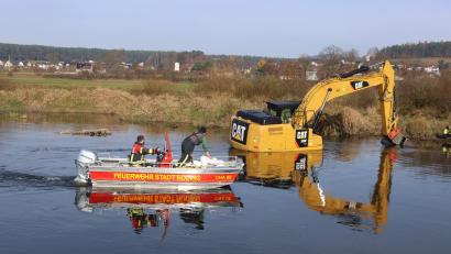Bild: Laube
Nach einem technischen Defekt an der Hydraulikleitung steckt der Bagger im Regen fest. Einsatzkräfte der Feuerwehr Roding sichten das Umfeld vom Rettungsboot aus.