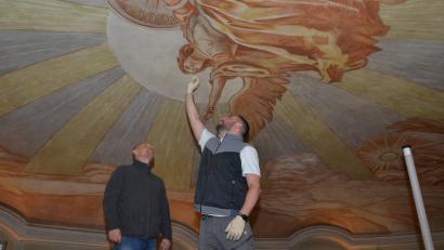 Bild: dob
Diplom-Restaurator Enrico Ferretti (rechts) wischt fast zärtlich über das Gesicht des Erzengels Michael, der in majestätischer Größe im Zentrum der Kuppel in der katholischen Stadtpfarrkirche schwebt. Kirchenmaler- und Vergoldermeister Martin Eis begutachtet das Werk.