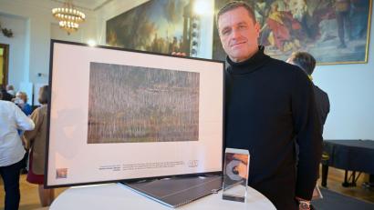 Bild: Malin Wunderlich/dpa
Der Münchner Fotograf Matthias Schrader steht mit seiner Auszeichnung für das Pressefoto des Jahres 2025 bei der Preisverleihung „Pressefoto Bayern 2025“ im Bayerischen Landtag. Schraders Bild zeigt eine Dampfeisenbahn in einem von Borkenkäfern befallenen Wald im Harz.