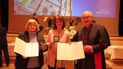 Bild: Jakob Schötz
Margret Lukas-Fuchs (links) aus Moosbach und Christine Schwab (Mitte) aus Luhe-Wildenau erhalten aus der Hand des Diözesanbischofs Dr. Rudolf Voderholzer die Wolfgangsmedaille.