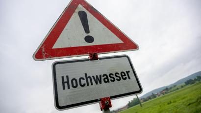 Symbolbild: Pia Bayer /dpa
Regentropfen hängen an einem Schild, das vor Hochwasser warnt. In Wernberg-Köblitz ist die Brückenstraße wegen Überschwemmung gesperrt.