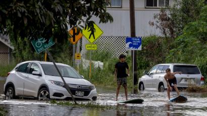 Bild: Stephen Lam/San Francisco Chronicle via AP/dpa
Zwei Jugendliche surfen in Waialua neben einem liegengebliebenen Fahrzeug im Hochwasser.