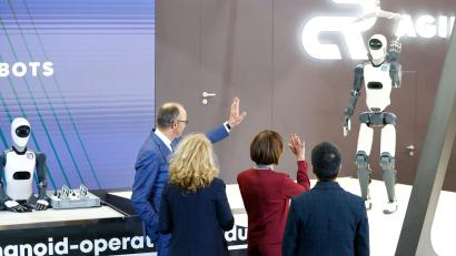 Bild: Michael Matthey/dpa
Bundeskanzler Friedrich Merz winkt einem Roboter zu – die Zukunft winkt zurück.