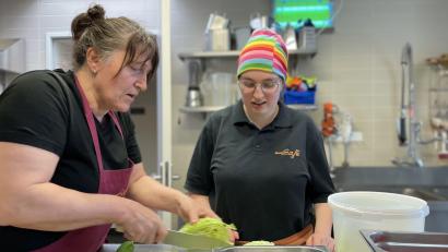 Bild: Paulina Schmidt
Vormittags bereiten die Mitarbeitenden alle Zutaten vor, die sie für kleine Beilagensalate brauchen. Uschi (links) zeigt Anna, wie sie den Salat dafür schneiden soll.