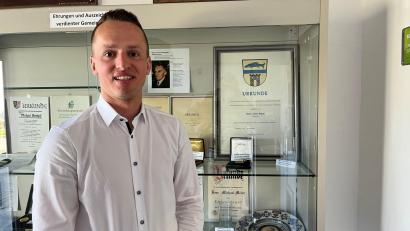 Bild: ihl
Der neue Bürgermeister von Schmidgaden, Martin Bauer, steht vor der Vitrine im Eingang zum Rathaus. Im Hintergrund ein Bild seines Urgroßvaters Josef Bauer. Er war ebenfalls Bürgermeister von Schmidgaden und ist Ehrenbürger. Martin Bauer heißt mit zweitem Vornamen Josef wie sein Urgroßvater.