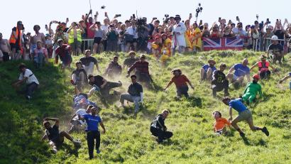 Bild: Jacob King/PA Wire/dpa
Kurioser Kultlauf in Gloucestershire: Beim Käserennen 2026 rennen Männer dem rollenden Käselaib den Hügel hinunter nach.
