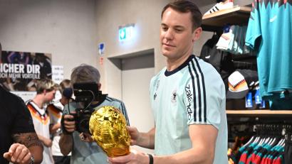 Bild: Federico Gambarini/dpa
Lächelnd signiert Manuel Neuer einen goldenen WM-Pokal.