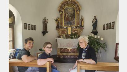Bild: Veronika Kreuzer
Rita Kreuzer in der Kapelle, um die sie sich schon seit vielen Jahren kümmert. Mit den Enkeln Konstantin und Johann (von links) ist schon die nächste Generation bereit. Am Altar stehen die Figuren des heiligen Michael (links) und der heiligen Margareta (rechts). An den Wänden sind auf einem Sockel Statuen des heiligen Antonius (links) und der Muttergottes (rechts) angebracht.