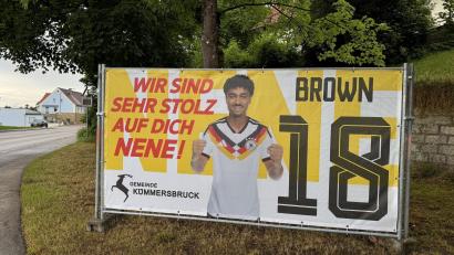 Bild: Heike Unger
Kümmersbruck feiert "seinen" Nationalspieler Nathaniel "Nene" Brown: Pünktlich zu Beginn der Fußball-Weltmeisterschaft 2026 verkündet seit 11. Juni Browns Heimatgemeinde Kümmersbruck per Transparent am Ortseingang in Lengenfeld im XL-Format "Wir sind sehr stolz auf dich Nene!".