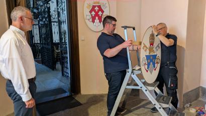 Bild: Paul Zrenner
Beim rechten Seiteneingang zur Basilika wurde ein geeigneter Raum für die Papstwappen-Galerie gefunden. Von links Pfarrer Dr. Thomas Vogl zusammen mit Mesner Dominik Sirtl und Johann Schnur, die die Wappen am Freitag zusammen mit Hubert Heinzl aufhängten.