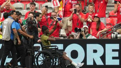 Bild: Abbie Parr/AP/dpa
Im Rollstuhl: Koné wird im Stadion begrüßt.
